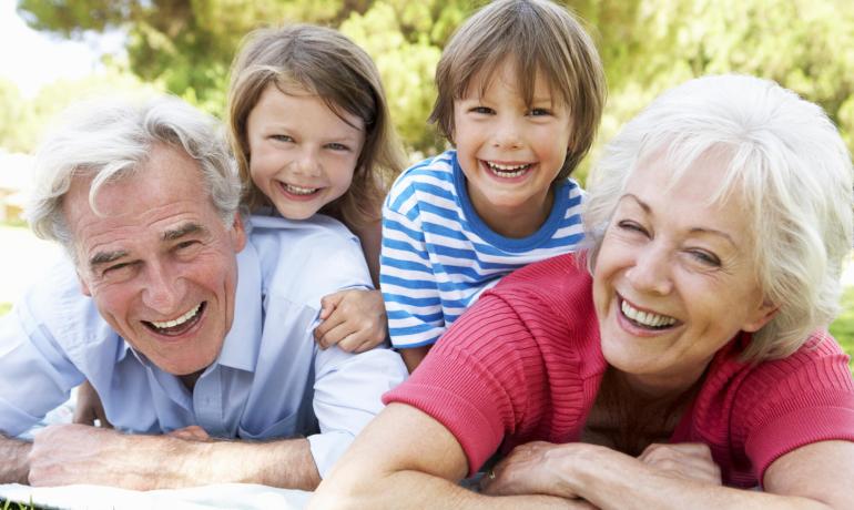 Nonni e nipoti sorridenti sdraiati sull'erba in un giorno di sole.