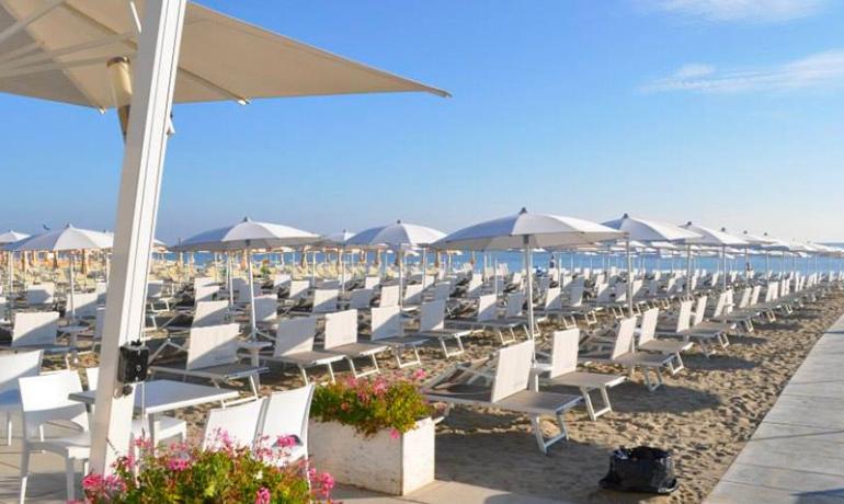 Beach with white sunbeds and umbrellas, clear sky.
