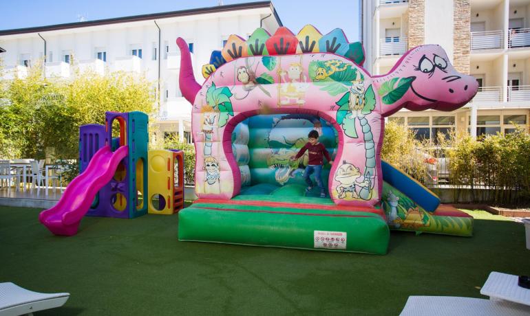 Parco giochi con gonfiabile a forma di dinosauro e scivolo colorato.