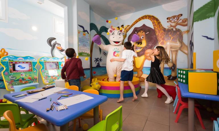 Enfants jouant dans une salle de jeux colorée avec un personnage en costume.