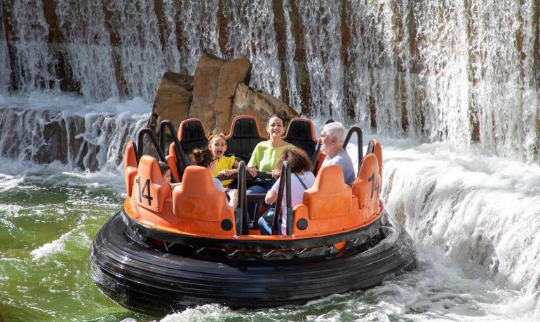 Glückliche Familie auf Wasserfahrt, Lachen und Spritzen unter Wasserfall.