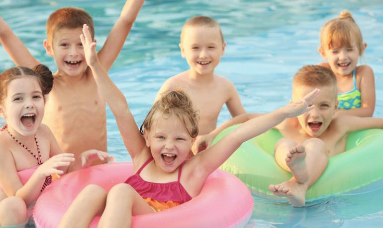 Bambini felici giocano in piscina con ciambelle colorate.