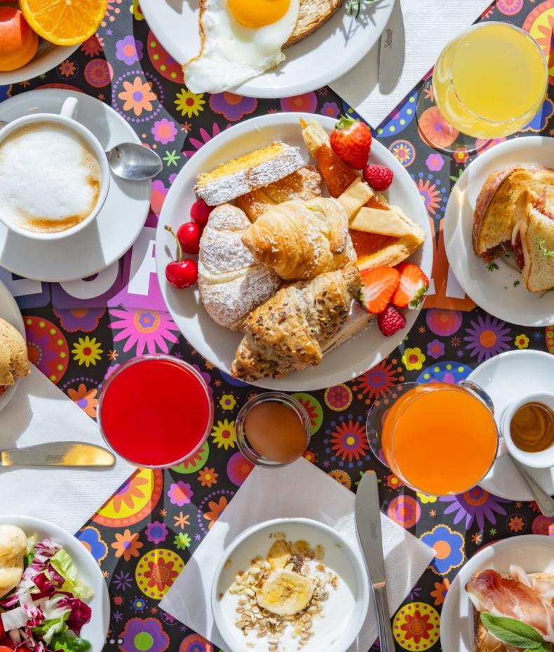 Petit-déjeuner coloré avec viennoiseries, fruits, œufs et boissons.