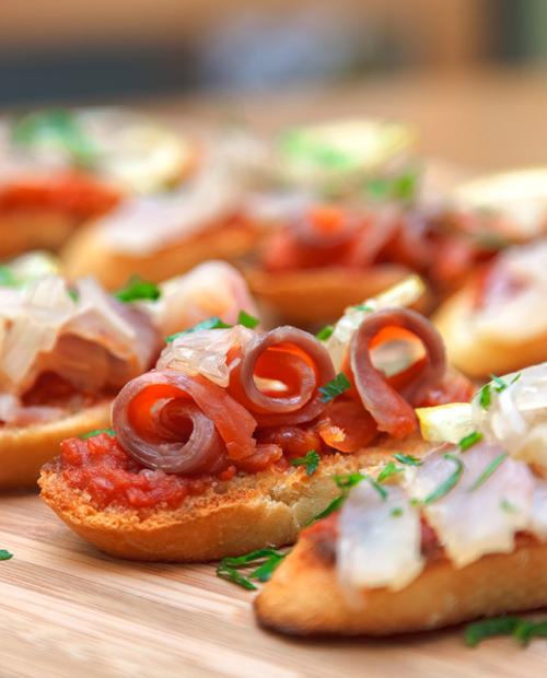 Crostini colorés avec tomate, oignon et anchois sur une planche en bois.