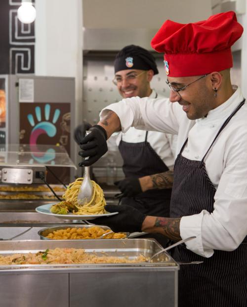 Des chefs souriants servent des pâtes avec enthousiasme et passion dans une cafétéria accueillante.