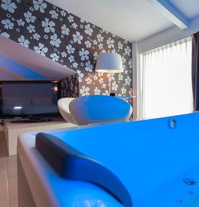 Relaxing blue bathtub in modern room with lamp and floral wallpaper.